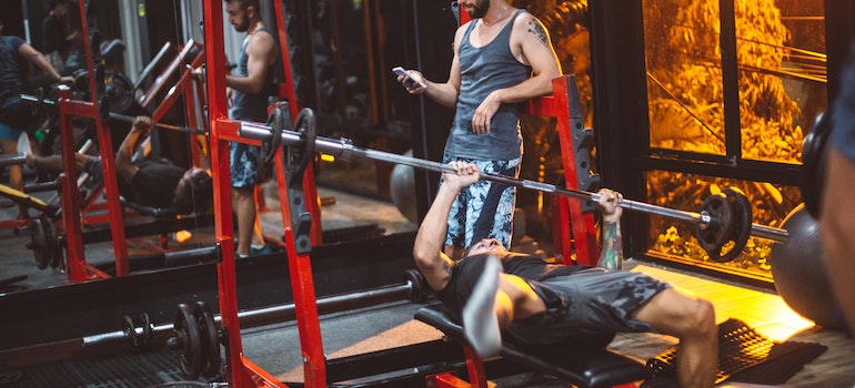 a guy in gym with a tracking app on a smartphone screen, highlighting the significance of monitoring and celebrating every achievement in exercise for recovery and sobriety