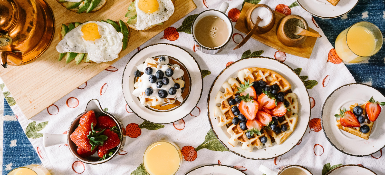 On a table, there is a variety of foods, including pancakes, drinks, eggs, strawberries and more.