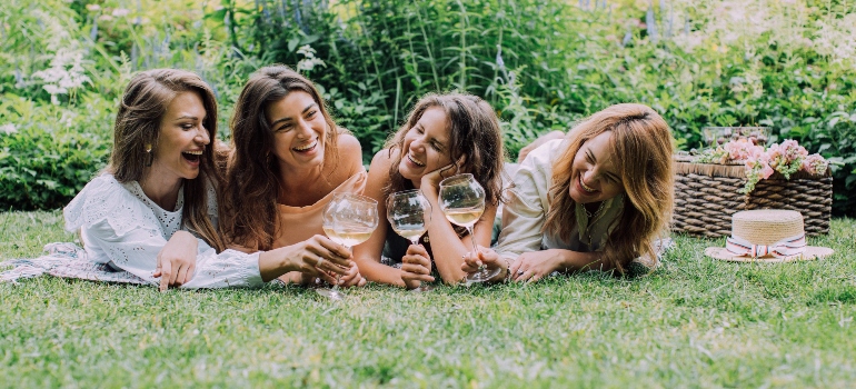 Four women drinking white wine while laying on the grass talking about Wine Mom Culture in Marietta OH