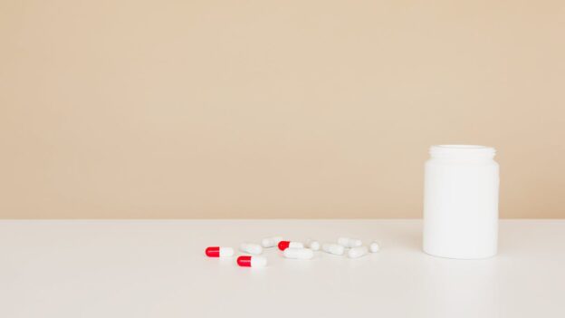 Red and white pills on a beige surface next to a white bottle