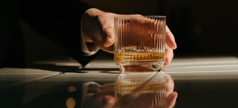 Close-up of a person's hands reaching for a glass of alcohol