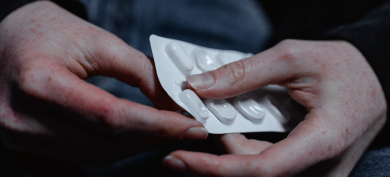 A person's hands taking a pill from a blister pack representing Opioid overdose prevention.