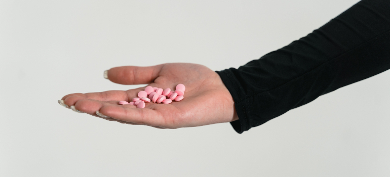 A hand holding a cluster of pink pills, symbolizing a critical point in the opioid withdrawal timeline.