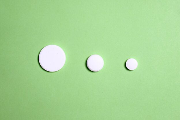 Three white round pills arranged from the biggest to the smallest on a green surface.