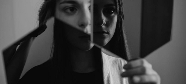 A person coping with psychosis looking at her face in two mirrors. 