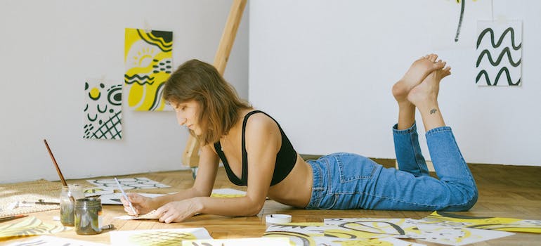 A woman lying on the floor and drawing with many papers lying around her