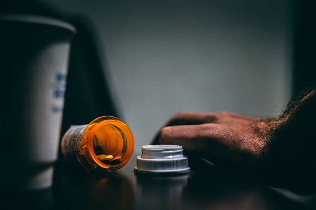 An empty medication bottle and a hand next to it