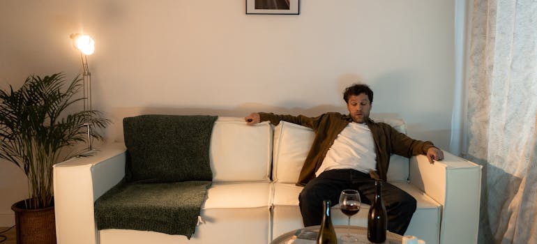 Intoxicated man sitting on the couch and drinking wine.
