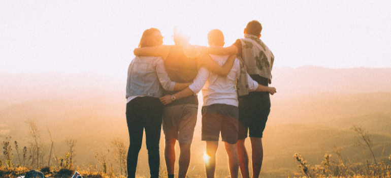 A group of four friends in a hike. We see their backs as they look towards the sunset.