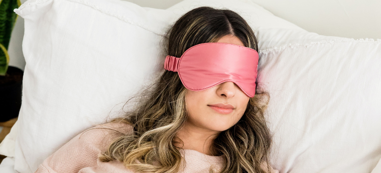 A young woman with a pink silk sleep mask is in bed