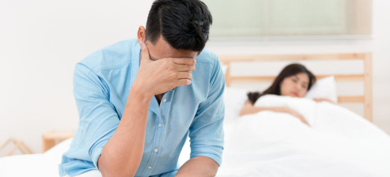 A man is preoccupied in the bed while his lover looks at him from afar. He may be preoccupied with the impact of sex addiction on mental health and relationships.