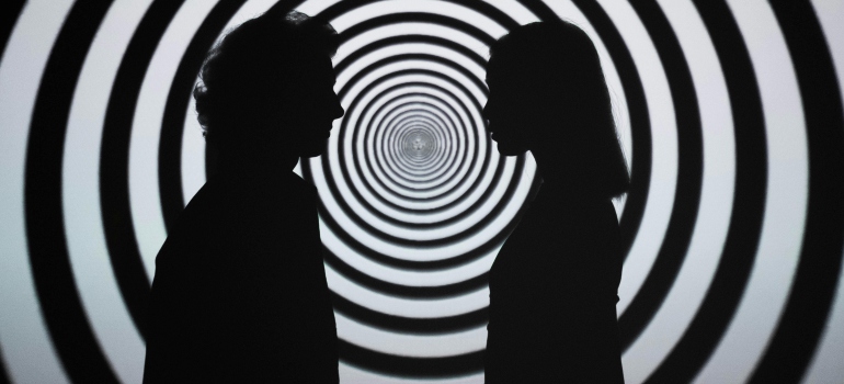 Silhouette of 2 people standing in front of white and black stripe wall symbolizing hallucinations