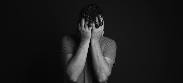 A guy in black and white covering his face with both hands, struggling with mental health