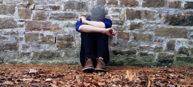 A boy sitting on a ground leaning against wall