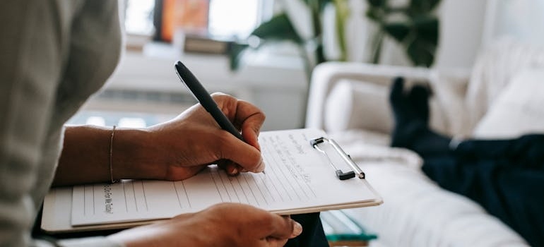 Therapist writing on a clipboard and telling her patient about the benefits of psychiatric care during addiction treatment in WV.