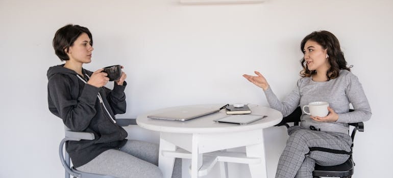 Two friends sitting at a table and talking while drinking coffee.