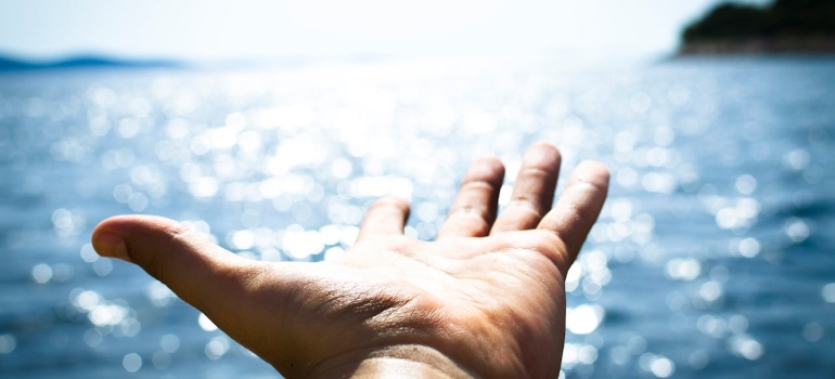 A hand reaching out to sun and seaside symbolizing hope