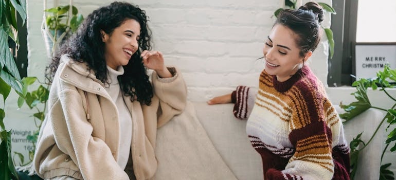 Two women sitting on a couch and laughing.