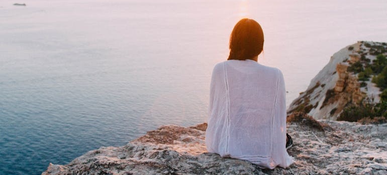 Woman sitting on a cliff looking at the sea.