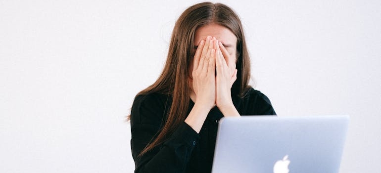 Woman covering her face in front of her laptop.