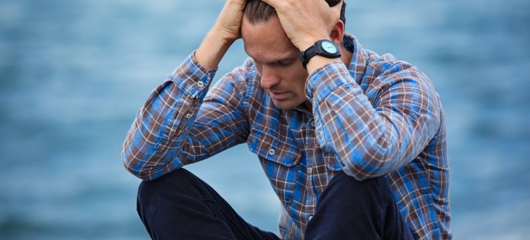 A troubled man sitting and putting his hands on his head nervously