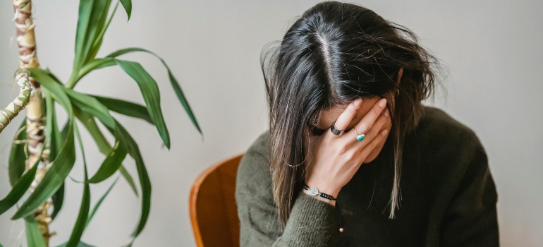 Worrying woman in grey jumper, covering her face, dealing with addiction and mental health.