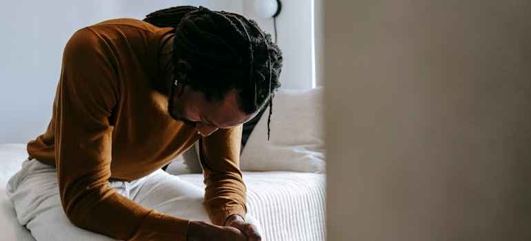 Man sitting on the bed with his head held down.