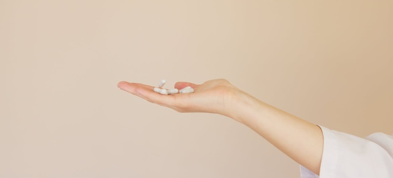 A woman holding pills on the pink background