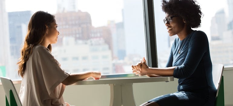 Two friends sitting at a table and talking to each other.