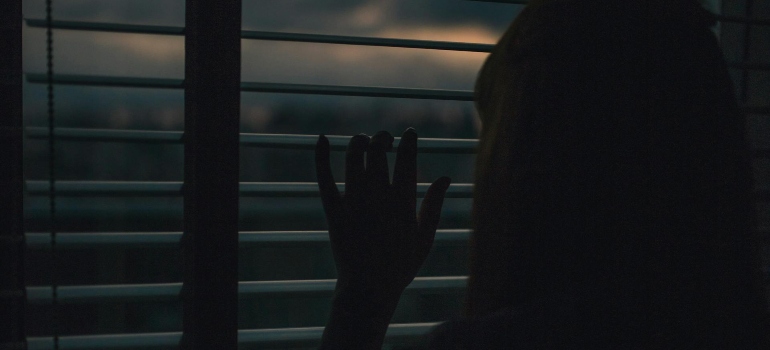 Woman looking through the window blinds.