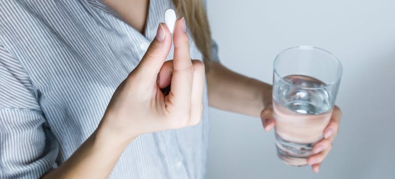 Woman holding a glass of water and taking a pill.