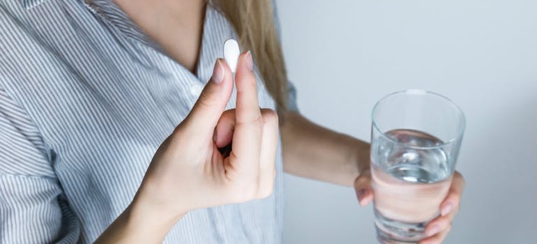 Woman holding a glass of water and a pill.