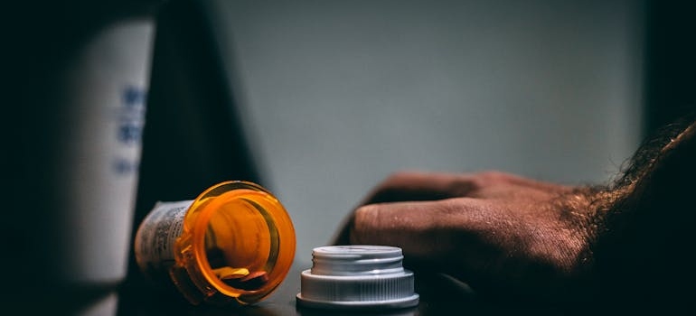 Man's hand next to a spilled bottle of pills.