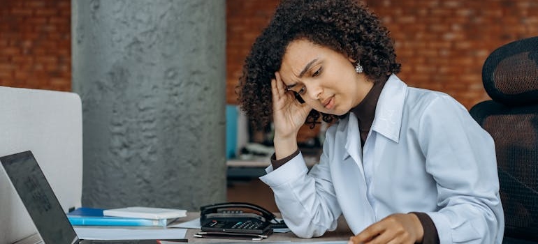 Woman holding her head and looking at her laptop.