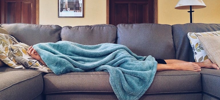 Woman lying on the couch covering her face with a blanket.