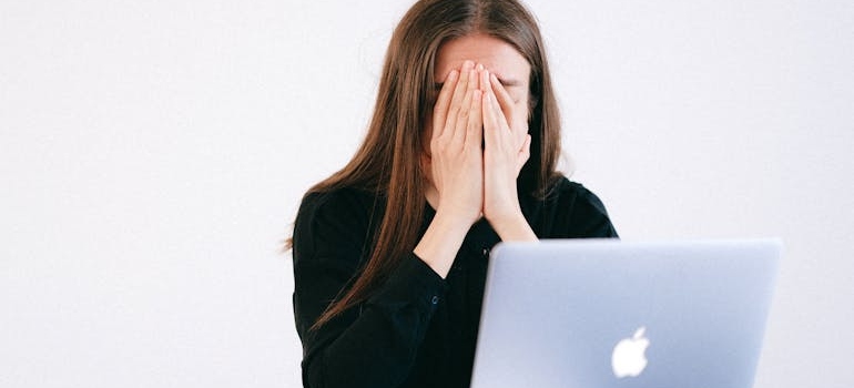 Woman covering her face while looking at a laptop.