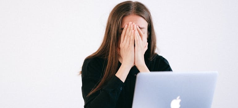 Woman covering her face while looking at her laptop.