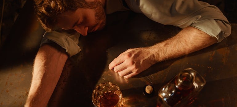 Man lying on the table while drinking whiskey.