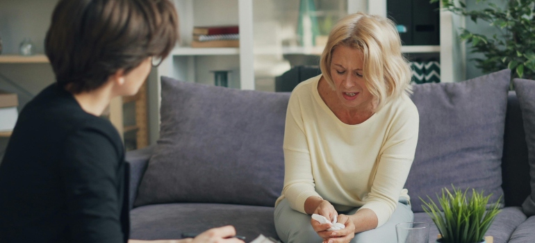 A woman is sitting on the couch and talking to her therapist about what rehab therapy can lead to success in overcoming addiction.