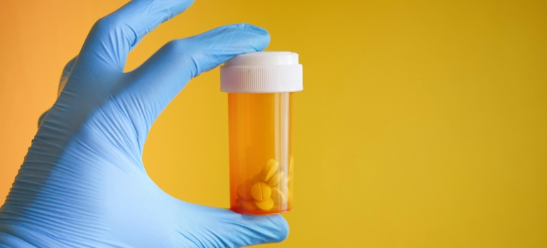 Tablets in orange plastic bottle, in a human's hand.