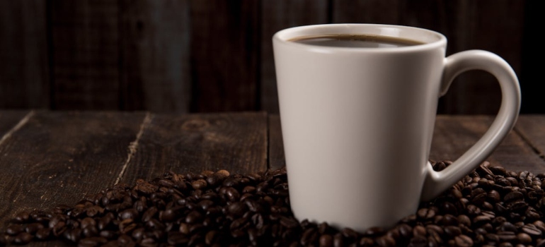 A cup of coffee surrounded by coffee beans