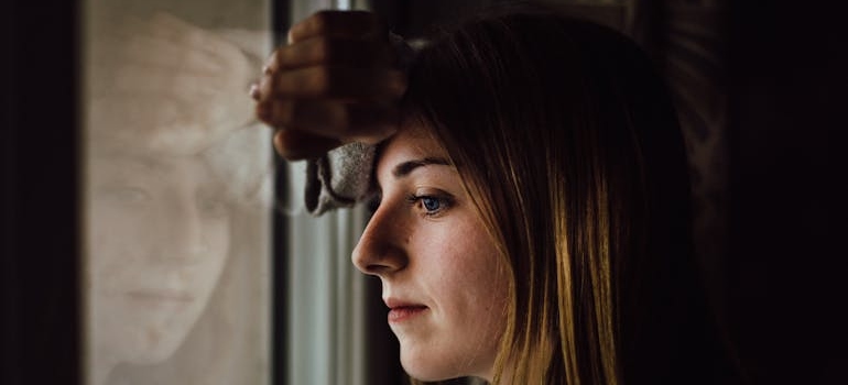 Woman looking out the window while holding her head.