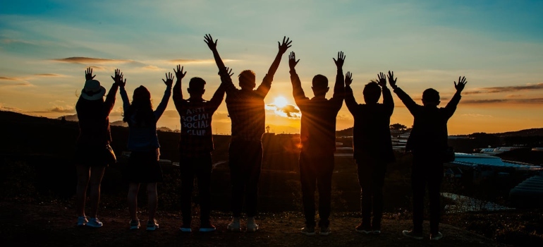 people with raised hands looking at the sunset