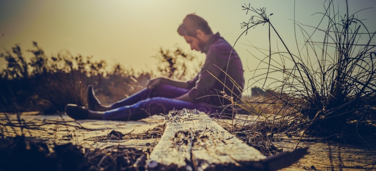 a lonely man sitting on the ground and thinking about Addiction Stigma in West Virginia’s Small Towns