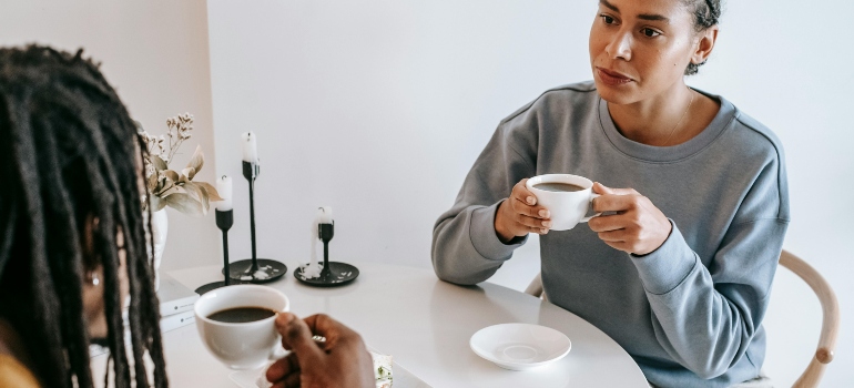 A woman is sitting at the table, holding a cup of coffee, and discussing with a man about how to rebuild trust with family and friends after addiction.