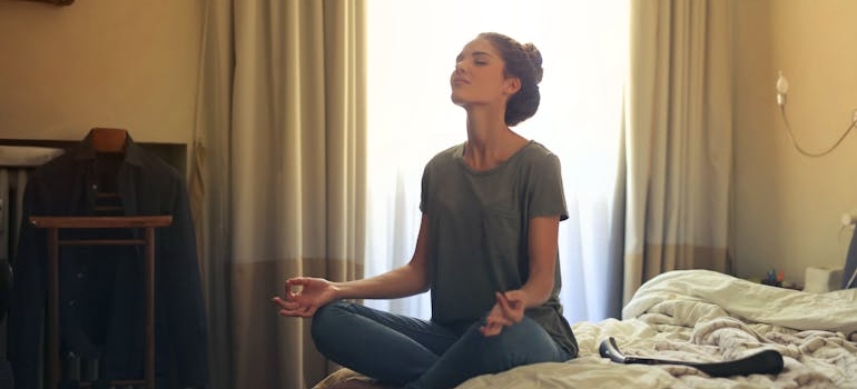 Woman sitting on a bed and meditating as a part of maintaining motivation throughout your recovery process.