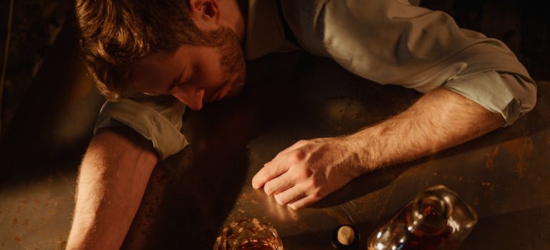 Man sleeping on a table while drinking whiskey.