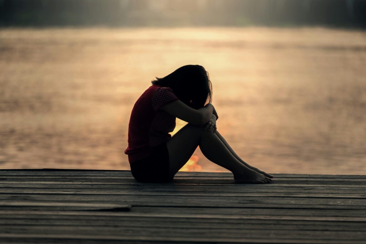 A depressed woman is sitting near the lake.