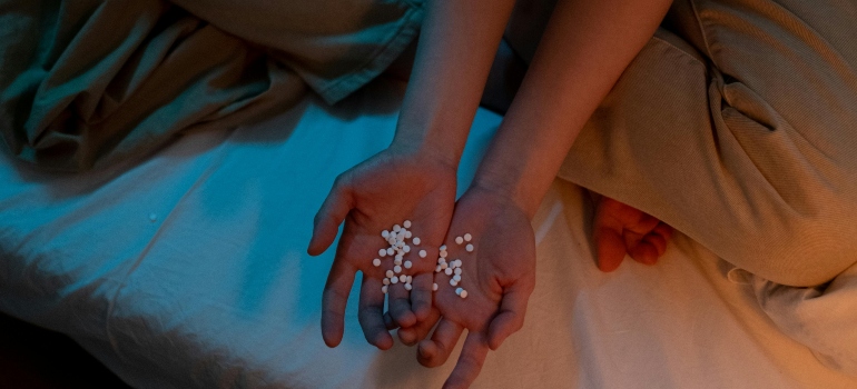 A woman is sitting on the bed and holding pills in her palms.