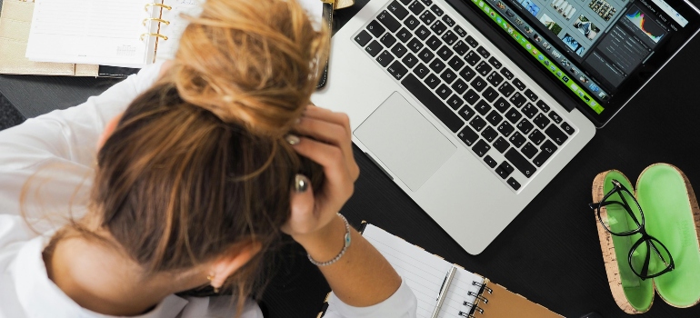 A stressed woman holding her head and thinking about substance abuse in the workplace.